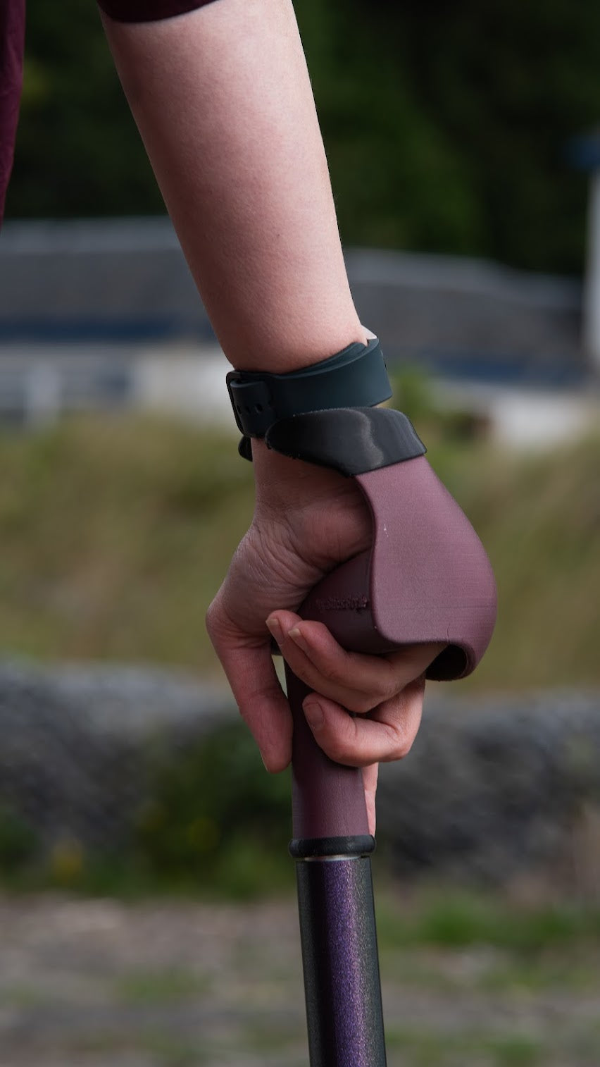 Hand holding a maroon red ergonomic walking stick handle with a purple cane with a blurred countryside background